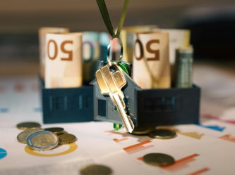 A house shaped keychain with a bunch of money in front of it