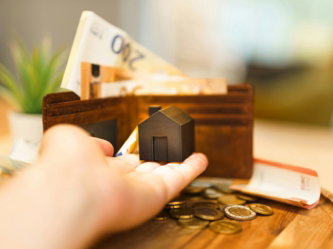 a-person-holding-a-small-house-and-some-money.jpg A person holding a small house and some money